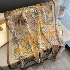 Elegant champagne silk scarf with floral and SS patterns on a beige leather sofa