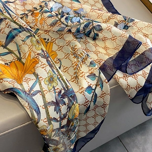 Macro detail of silk scarf showing floral lily prints and decorative S logo pattern