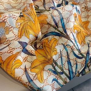 Detail of floral print silk scarf featuring orange lilies and luxury logo pattern