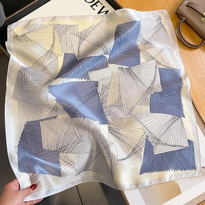 Elegant geometric silk square scarf in blue and beige draped on a wooden surface