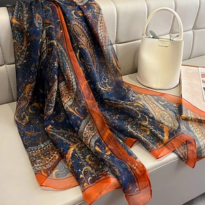 Detail of paisley pattern silk scarf in navy blue and orange draped on a beige sofa