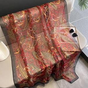 Long red paisley silk scarf for women laid on a sofa, perfect for summer sun protection