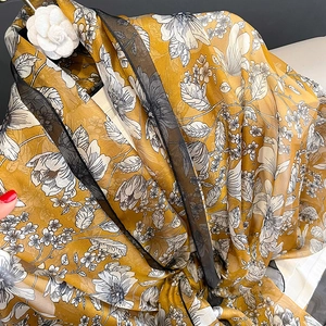 Detail of elegant yellow floral silk scarf with thin black borders and camellia accessory