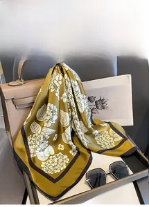 Detail of elegant dark green silk scarf with white floral print draped on a leather bag