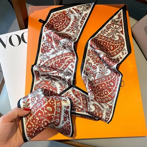 Detail eines rot-weißen Seidenschals mit Paisley-Muster auf einer orangefarbenen Box