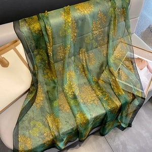 Dark green floral print silk scarf with golden chrysanthemums on grey sofa background