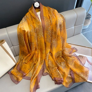 Elegant floral silk scarf in orange and gold with dark borders on a stylish sofa