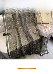 Detailed close-up of dark grey floral silk scarf draped elegantly on a white leather sofa