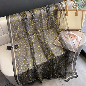 Floral print long scarf in black and yellow chiffon fabric styled on a leather sofa