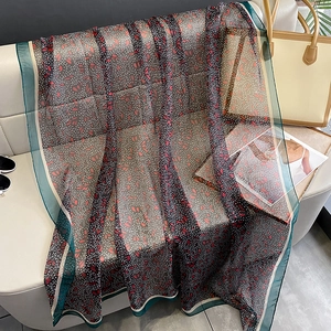 Floral chiffon scarf with dark green border and red flowers on a leather sofa