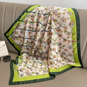 Carré de soie à fleurs et papillons avec bordure verte posé sur un canapé chic