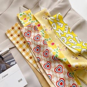 Flat lay of multiple printed narrow silk scarves on a beige suit and fashion magazine