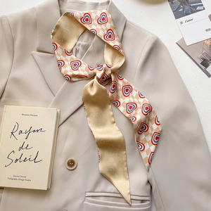 Fashionable narrow silk scarf with red heart prints tied on a beige blazer collar