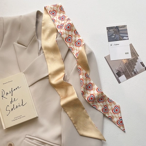Close-up of narrow silk scarf featuring checkerboard heart patterns and script text