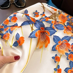 Detailed close-up of silky floral scarf with blue and orange prints on cream fabric