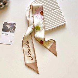 Detailed view of elegant long floral silk scarf tied to a bag handle in soft cream