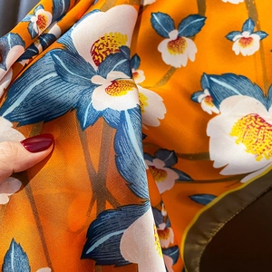 Detailed macro view of orange silk scarf with floral print and smooth texture