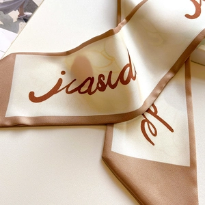 Macro view of silky twilly scarf with beige base, brown edges and artistic lettering