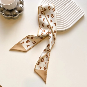 Detail view of a beige silk twilly scarf with brown numeric print and contrast borders