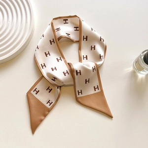 Detailed view of beige silk twill scarf with caramel H-pattern print on a white tray