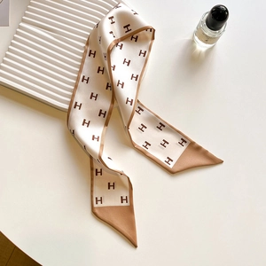 Detailed close-up of a narrow beige silk scarf featuring dark brown H letter patterns