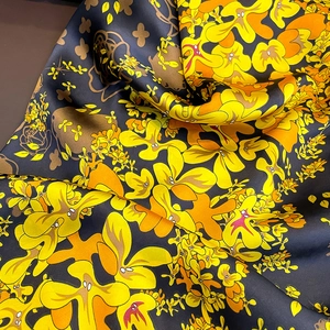 Elegant black silk scarf with vibrant yellow floral patterns and smooth satin texture