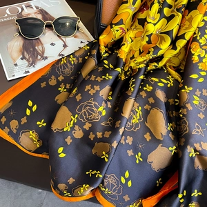 Elegant black silk scarf with yellow floral prints and sunglasses on a stylish desk