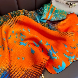 Vibrant orange silk scarf featuring blue bird patterns and a smooth, lustrous drape