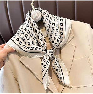 Detail of luxury geometric logo pattern on cream silk scarf styled with a beige blazer
