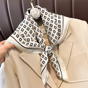 Elegant off-white silk scarf with black monogram pattern styled on a beige suit lapel