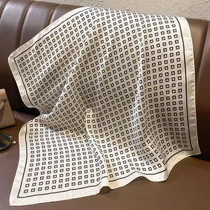 Detail of square silk scarf with geometric print draped over a leather sofa