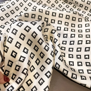 Detailed macro view of cream satin silk scarf with vintage black G geometric pattern