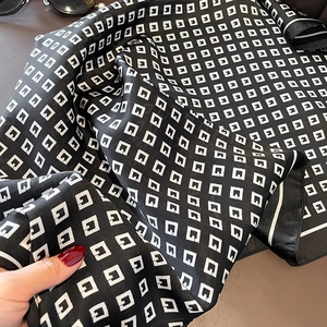 Macro detail of silk-feel scarf fabric featuring black and white geometric pattern