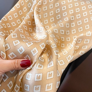 Macro detail of champagne satin silk scarf showing geometric G-letter pattern texture