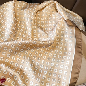 Detail of champagne gold silk scarf featuring classic monogram patterns and dark brown edges