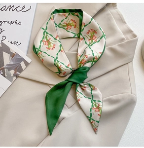 Detail of elegant green floral twilly silk scarf tied on a beige suit jacket