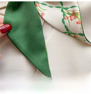 Detail of green floral silk scarf tied on a beige blazer sleeve with premium satin texture