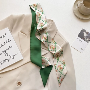 Close-up of green lily print silk scarf styled on a beige blazer with French accessories