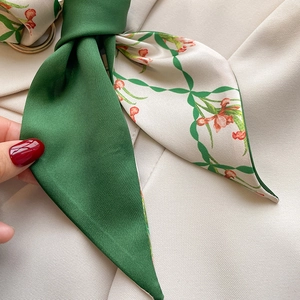 Detail of green and floral double-sided silk scarf with gold ring on beige blazer