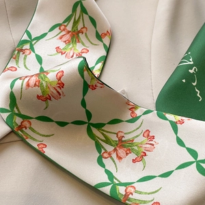Detail of floral green silk scarf tied on a beige blazer collar with orchid pattern