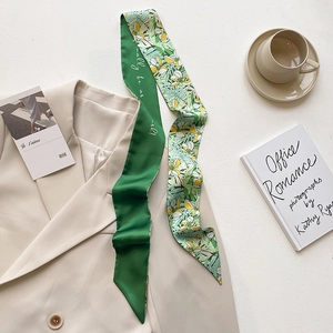 Detail of double-sided green floral silk scarf styled on a beige blazer and accessories