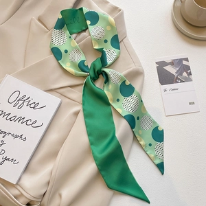 Detail of green polka dot silk twilly scarf knotted on a beige blazer for office style