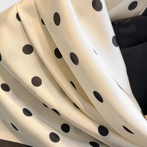 Gros plan sur un tissu satiné soyeux à pois noirs montrant un drapé fluide doux