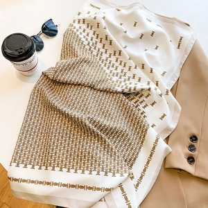 Close-up of pearl white silk scarf with gold TB monogram pattern on a khaki blazer