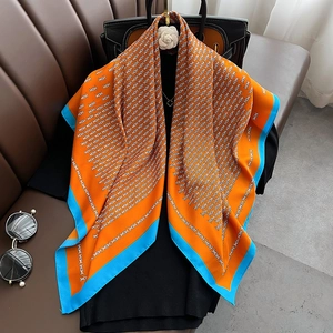 Orange silk square scarf with geometric patterns draped over a black mannequin top