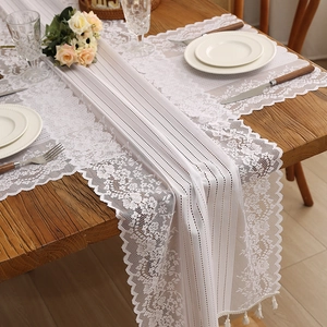 White lace table runner with hollow floral pattern and fringes on a wooden dining table