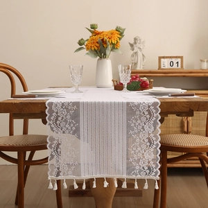 White lace table runner with hollow floral embroidery and tassels on a wooden dining table