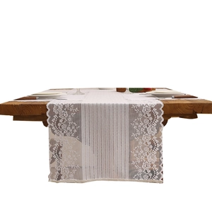Vintage white lace table runner with floral embroidery and tassel on dark wood table