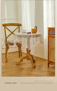 Detailed close-up of white floral lace tablecloth with scalloped edges on a wooden table
