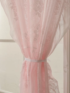 Detail of pink French lace curtain with floral patterns and a decorative white ribbon